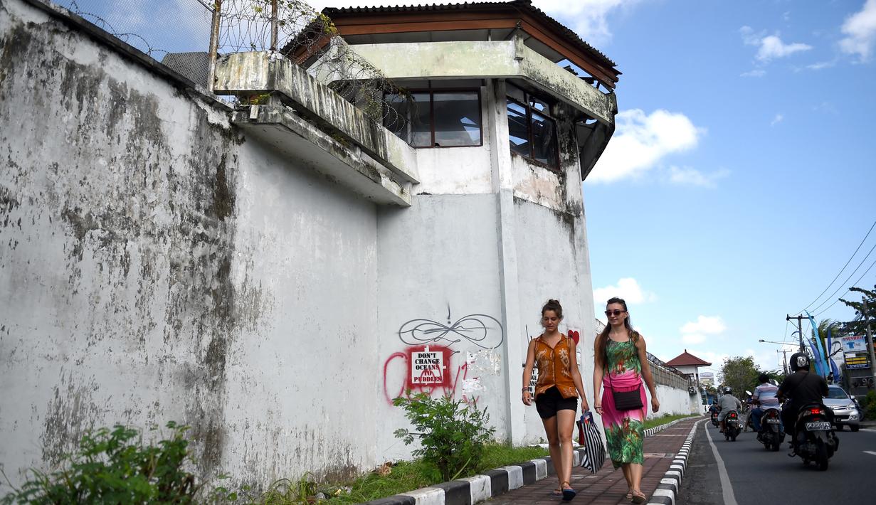 Dua turis asing berjalang di sepanjang dinding parimeter Lembaga Pemasyarakatan (Lapas) Kerobokan, Bali, Senin (19/6). Empat narapidana asing kabur melalui lubang sepanjang 15 meter yang mengarah ke parit di luar bangunan Lapas. (SONNY TUMBELAKA/AFP)