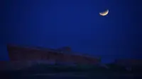 Bulan purnama yang sebagian gerhana terlihat tepat sebelum terbenam di belakang Holocaust Memorial di Montevideo, Uruguay pada Rabu (26/5/2021). (Mariana SUAREZ / AFP)