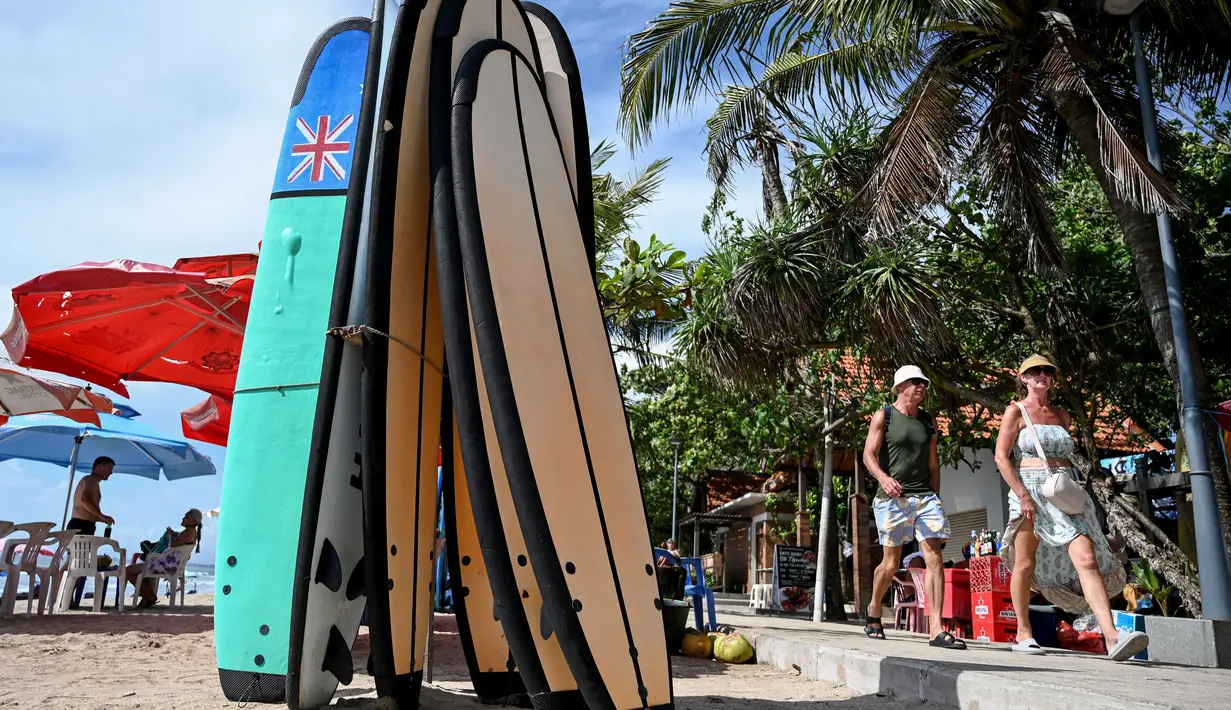Wisatawan berjalan melewati papan selancar di pantai Kuta, Bali, pada tanggal 8 Desember 2023. (SONNY TUMBELAKA/AFP)