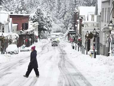 Seorang warga berjalan saat hujan salju di sepanjang Broad Street di Nevada City, California (27/12/2021). Hujan salju dingin membuat perjalanan hampir tidak mungkin dilakukan di beberapa bagian California, Nevada. (Elias Funez/The Union via AP)