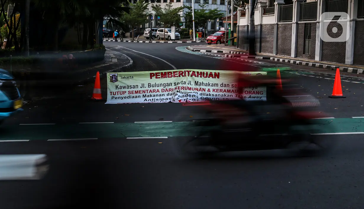 Pengendara melintasi spanduk pemberitahuan penutupan area kawasan Taman Ayodya, Jalan Bulungan dan Mahakam, Jakarta, Rabu (23/9/2020). Penutupan jalan dilakukan agar masyarakat tidak berkumpul di area itu pada waktu malam hari dan guna menekan angka penularan COVID-19. (Liputan6.com/Johan Tallo)