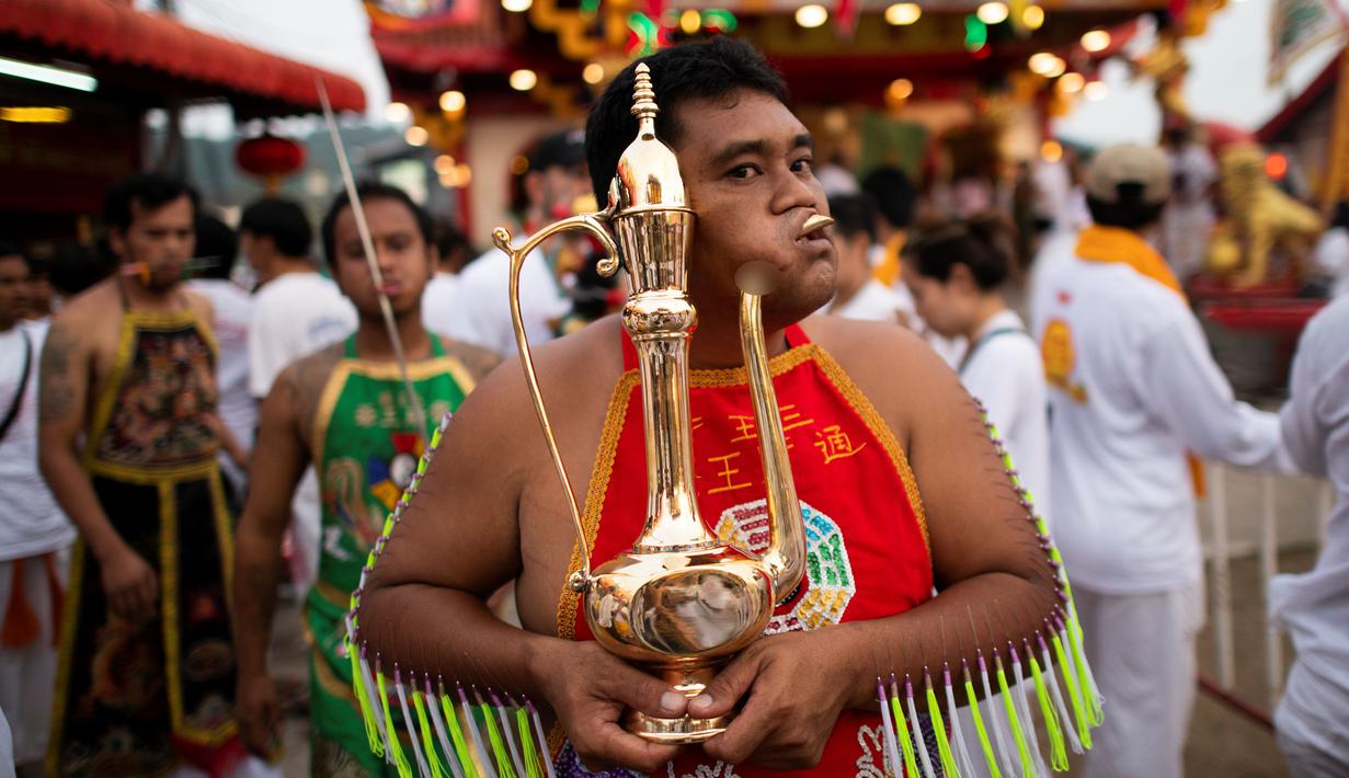 Penganut kuil Loem Hu Thai Su menusukkan menusukkan teko besi ke pipinya saat festival vegetarian tahunan di Phuket, Thailand, Jumat (12/10). Acara ini diselenggarakan oleh komunitas keturunan Tionghoa di seluruh Thailand. (Jewel Samad/AFP)
