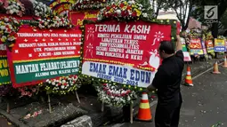 Seorang pria memegang karangan bunga di depan Gedung KPU, Jakarta, Sabtu (21/4). Karangan bunga di depan Gedung KPU terus bertambah setiap harinya. (Liputan6.com/JohanTallo)