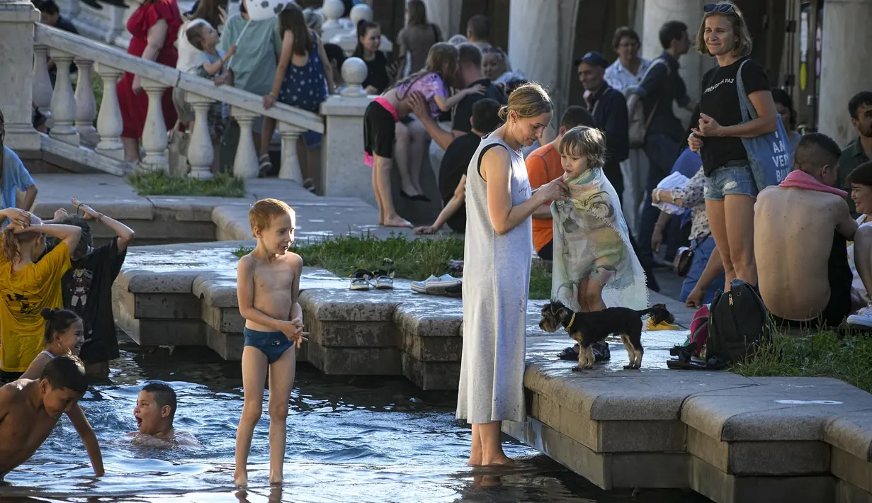 Seorang ibu menutupi anaknya dengan handuk setelah mandi di air Sungai Neglinnaya saat menikmati akhir hari yang panas di dekat Tembok Kremlin, Moskow, Rusia, 3 Juli 2022. Cuaca panas di Moskow datang dengan perkiraan suhu mencapai 30 derajat Celcius (86 Fahrenheit). (AP Photo/Alexander Zemlianichenko)