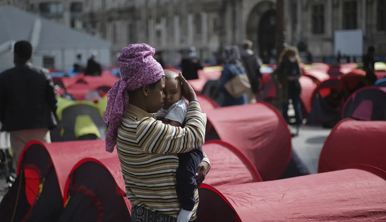 Seorang imigran perempuan menggendong banyinya di kamp darurat yang didirikan di luar balai kota Paris, Jumat (25/6/2021). Lebih dari 300 migran mendirikan sekitar 200 tenda di luar balai kota untuk menarik perhatian terhadap kondisi mereka dan menuntut akomodasi. (AP Photo/Lewis Joly)