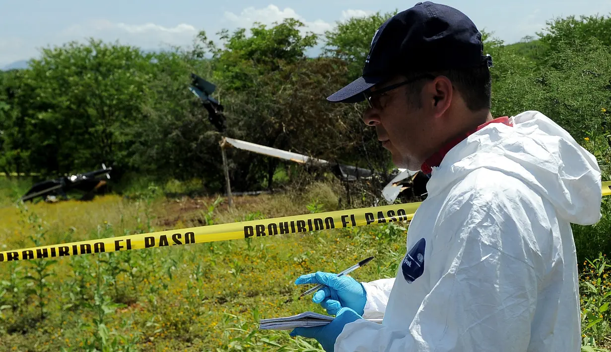 Petugas forensik berdiri di dekat puing helikopter polisi yang diduga jatuh ditembak oleh sekelompok geng kartel narkoba di Michoacan, Meksiko barat, Rabu (7/9). Insiden ini menyebabkan empat orang di helikopter tersebut tewas. (PEDRO PARDO/AFP)