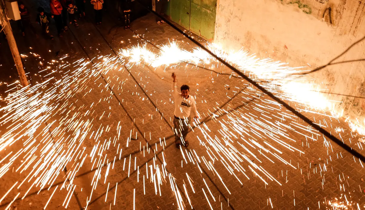 Seorang pemuda Palestina mengayunkan kembang api buatan sendiri, saat orang-orang merayakannya pada malam menjelang bulan suci Ramadan, di Kota Gaza (11/4/2021). (AFP Photo/Mohammed Abed)