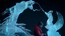 Seorang pemahat es memberikan sentuhan akhir pada patung es di festival Ice and Snow World Harbin, di Harbin, timur laut China, Jumat (3/1/2019). Festival es terbesar dunia ini diadakan untuk menyambut musim dingin yang berlangsung selama satu bulan lebih. (NOEL CELIS/AFP)