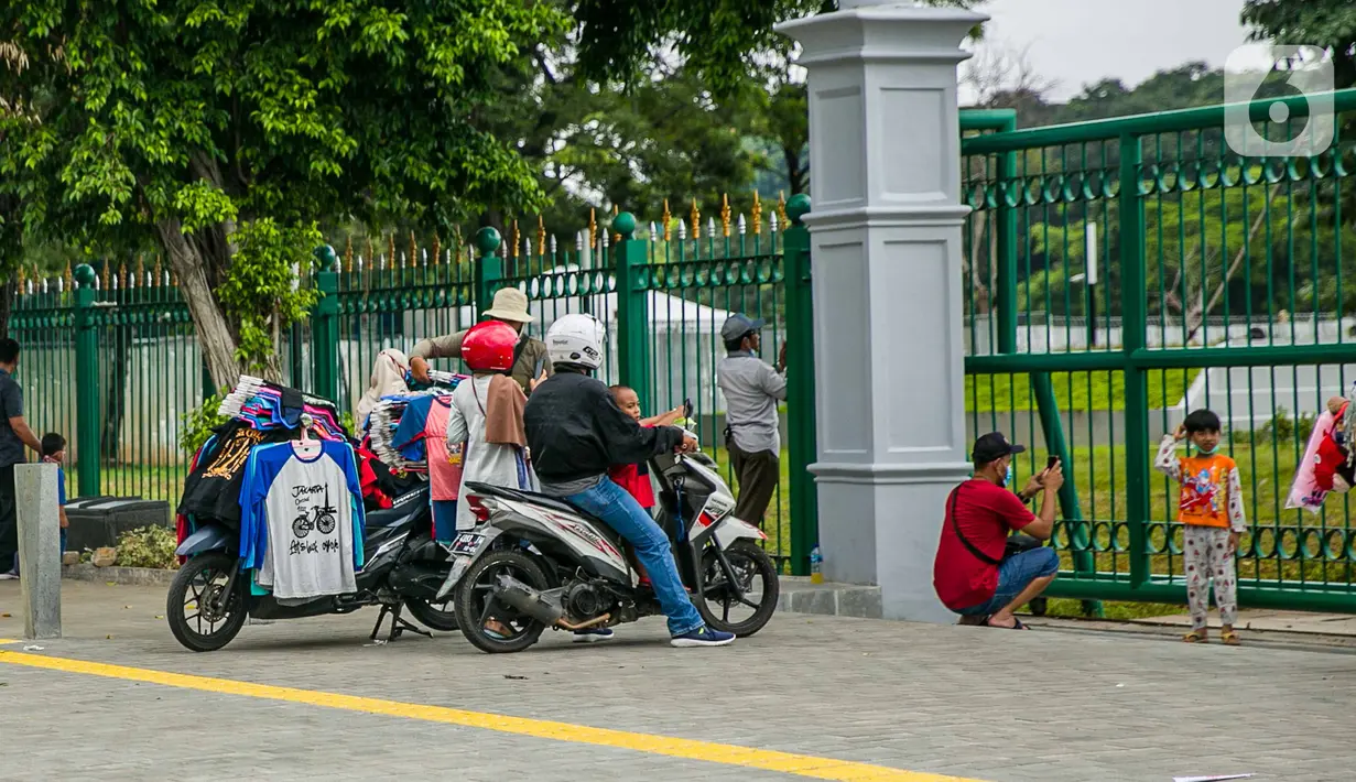 Pedagang kaos cendera mata keliling mencoba peruntungan dari para pengunjung yang ingin menyaksikan Tugu Monas Jakarta dari balik pagar, Sabtu (2/1/2021). (Liputan6.com/Faizal Fanani)