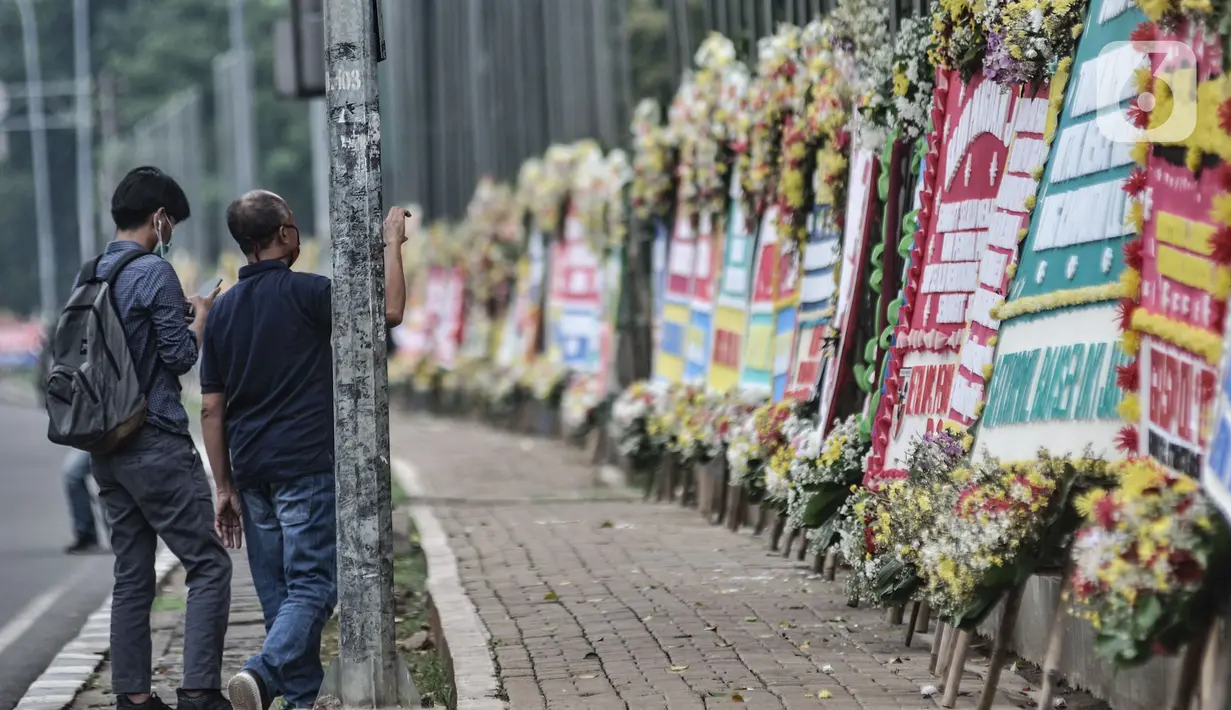 Pejalan kaki mengambil gambar karangan bunga yang dipajang di depan Markas Kodam Jaya, Jakarta, Senin (23/11/2020). Ratusan karangan bunga dikirim masyarakat sebagai bentuk dukungan terhadap TNI dan Polri atas tindakan tegas kepada pelanggar protokol kesehtan Covid-19. (merdeka.com/Iqbal S Nugroho)