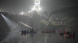 Tim penyelamat di kapal mencari di sungai Machchu di sebelah jembatan kabel yang runtuh di kota Morbi di negara bagian barat Gujarat, India, Senin, 31 Oktober 2022. Jembatan gantung kabel berusia seabad runtuh ke sungai Minggu malam, menyebabkan ratusan orang terjun. di dalam air, kata para pejabat. (AP/Ajit Solanki)