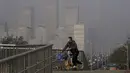 Seorang pria yang mengenakan masker untuk membantu mengekang penyebaran virus corona mengendarai sepeda di jembatan di atas gedung perkantoran di Central Business District yang diselimuti kabut polusi di Beijing, Kamis (18/11/2021).  (AP Photo/Andy Wong)