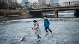 Dua orang anak asyik bermain ice skating atau seluncur es di atas sungai yang telah membeku di Beijing, Jumat (1/1). Semenjak membeku, sungai di Beijing ini menjadi objek wisata es dadakan yang banyak diminati wisatawan.  (AFP/Fred Dufour)