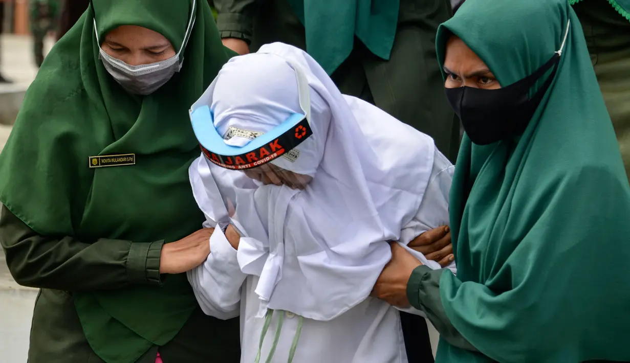 Polisi syariat membawa terpidana kasus zina untuk menjalani hukuman cambuk di halaman Masjid Al-Munawarah, Kota Jantho, Aceh Besar,  Jumat (9/4/2020). Pasangan terpidana yang terbukti melanggar Syariat Islam dalam kasus zina itu masing masing menjalani sebanyak 100 cambuk. (CHAIDEER MAHYUDDIN/AFP)