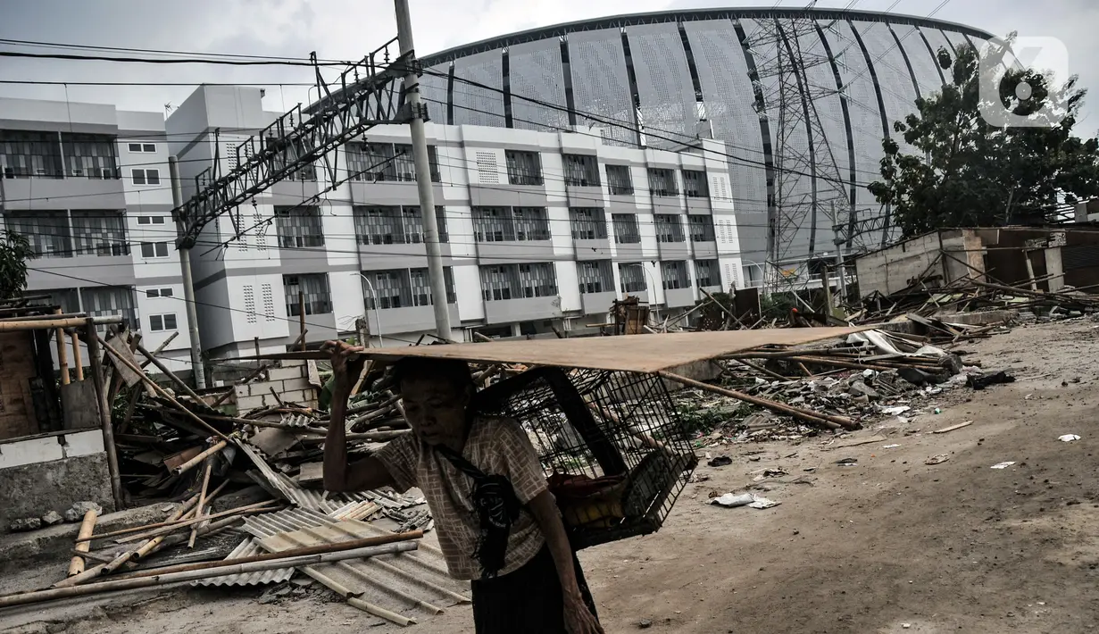 Warga membawa barang miliknya yang tersisa pascapenggusuran ratusan bangunan semipermanen di Kampung Bambu, Tanjung Priok, Jakarta Utara, Selasa (11/10/2022). PT KAI membongkar sekitar 254 bangunan semipermanen yang berada di bantaran rel atau dekat Jakarta International Stadium (JIS) guna sterilisasi jalur kereta api dan pembangunan stasiun baru di kawasan tersebut. (merdeka.com/Iqbal S. Nugroho)