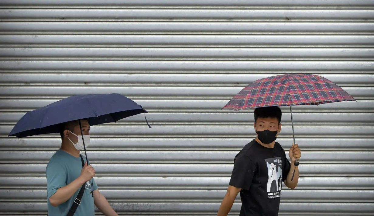 <p>Komuter mengenakan masker dan membawa payung berjalan selama jam sibuk pagi hari pada hari hujan di Beijing, Rabu (29/6/2022). China memangkas lama karantina wajib bagi pelancong luar negeri dari 21 hari menjadi tujuh hari ditambah tiga lagi pemantauan di rumah. (AP Photo/Mark Schiefelbein)</p>