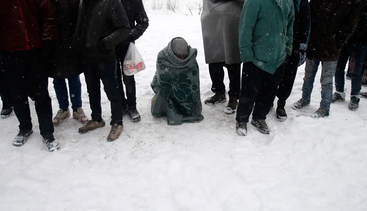 Seorang imigran tampak kedinginan saat mengantre makanan hangat di kamp pengungsian di Belgrade, Serbia (11/1). Para imigran tersebut sebagian besar dari Afghanistan dan Pakistan. (AP Photo/Darko Vojinovic)