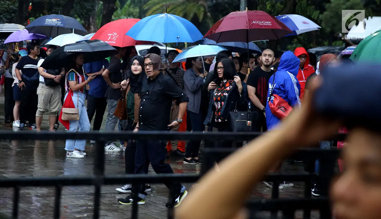 Penonton mengenakan payung karena hujan saat mengantre tiket masuk konser Liam Gallagher di Ecovention Ancol, Jakarta Utara, Minggu (14/1). Liam Gallagher siap menghibur para penggemarnya selama 90 menit. (Liputan6.com/JohanTallo)