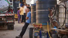 Warga Palestina berkumpul di samping gerobak yang ditarik keledai yang dimuat dengan tangki air untuk dijual. (MAHMUD HAMS/AFP)