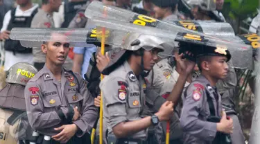 Petugas kepolisian menggunakan tameng untuk berteduh dari hujan saat menjaga aksi Hari Buruh di Jalan Medan Merdeka, Jakarta, Senin (1/5). (Liputan6.com/ Yoppy Renato)