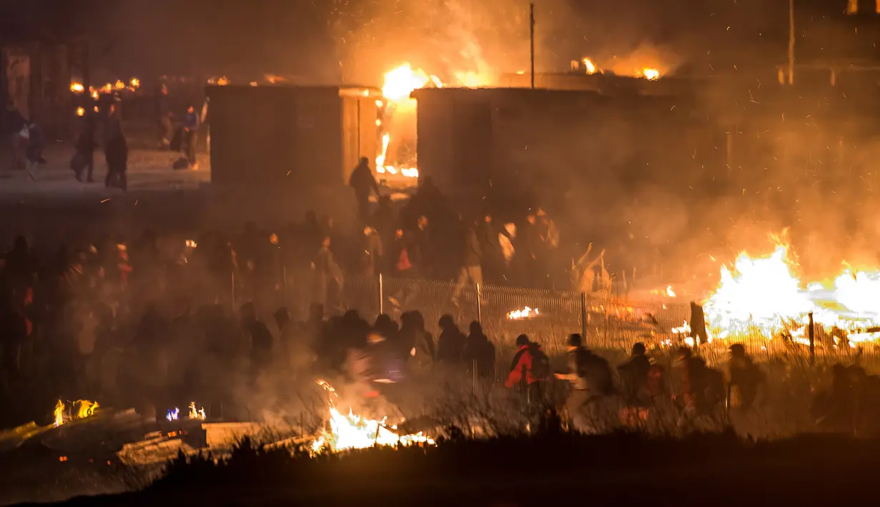 Imigran meninggalkan kamp penampungan mereka yang terbakar di Dunkirk, Prancis, Senin (10/4).  Di kamp penampungan ini setidaknya telah tinggal sebanyak 1500 imigran. (AFP PHOTO / PHILIPPE HUGUEN)