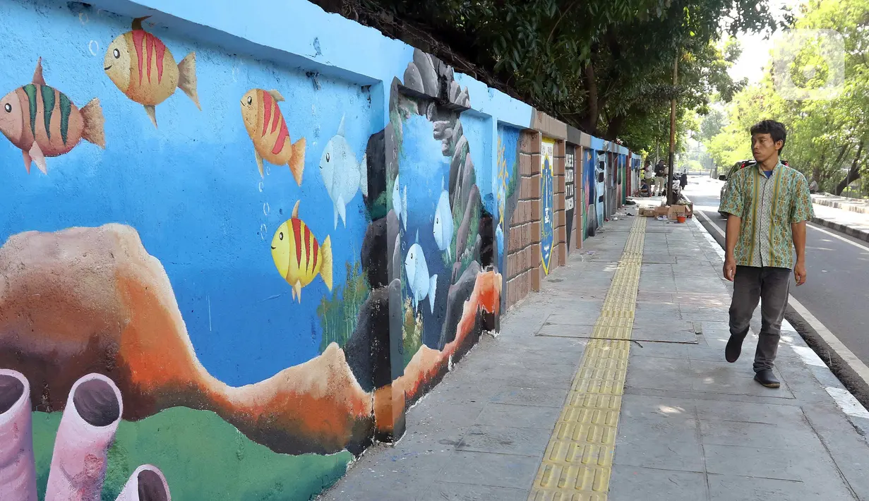 Warga berjalan di samping mural bertema biota laut yang menghiasi dinding di kawasan Cideng, Jakarta, Rabu (29/11/2023). Mural dibuat guna memperindah sekaligus penataan kawasan Kelurahan Cideng, Jakarta Pusat. (Liputan6.com/Herman Zakharia)