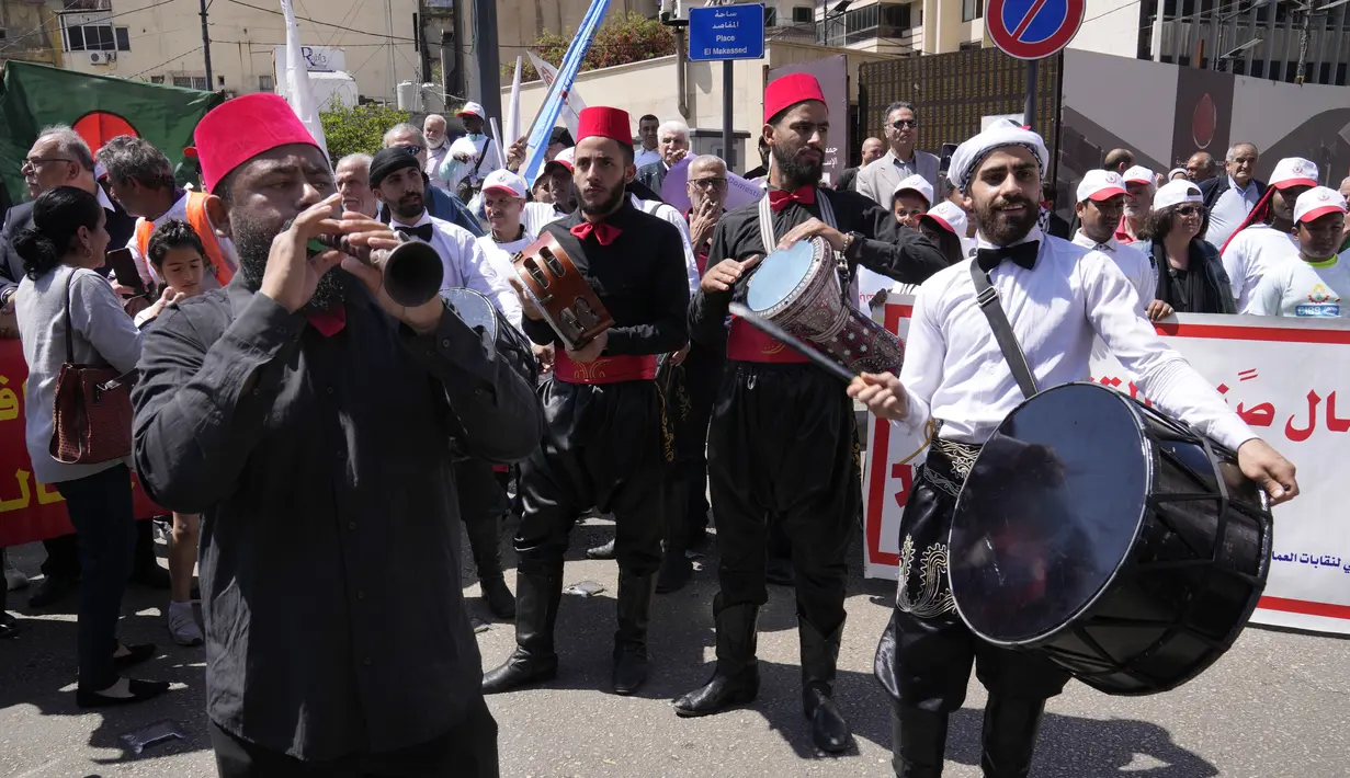 Pemain perkusi yang mengenakan pakaian tradisional Lebanon memimpin nyanyian pada pawai hari buruh tahunan di Beirut, Senin, 1 Mei 2023. Ratusan anggota Partai Komunis dan serikat buruh, serta sekelompok pekerja rumah tangga migran, berbaris melalui jalan-jalan di pusat kota Beirut.  (AP Photo/Hussein Malla)