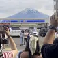 Para pengunjung mengambil foto di depan toko serba ada di kota Fujikawaguchiko, prefektur Yamanashi, Jepang, dengan latar belakang Gunung Fuji pada tanggal 28 April 2024. (Kyodo News via AP)