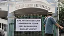Jemaah melintasi spanduk pemberitahuan yang dipasang oleh petugas di Masjid Jami'e Baitussalam, Cipinang, Jakarta, Jumat (10/4/2020). (merdeka.com/Iqbal S. Nugroho)