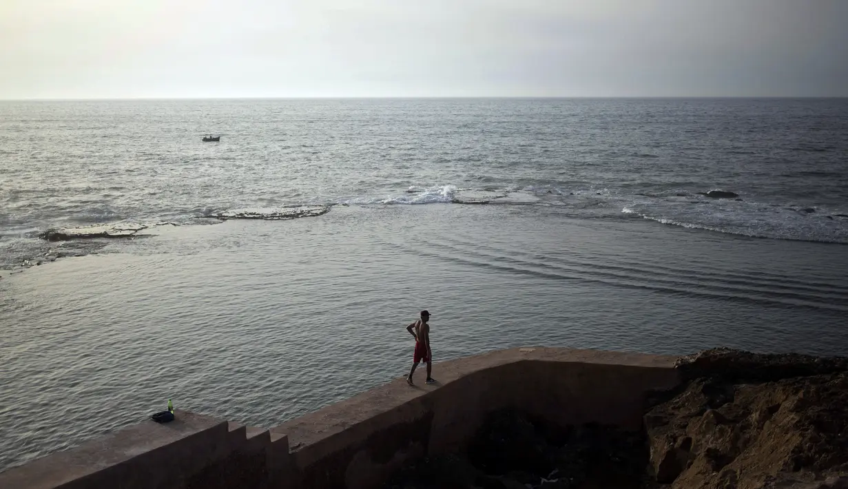 Seorang pria berjalan di sepanjang pagar sebelum melompat untuk berenang malam di Samudra Atlantik, di Rabat, Maroko, Selasa (22/9/2020). (AP Photo / Mosa'ab Elshamy)