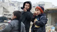 Dua orang anak makan roti sambil menunggu untuk dievakuasi dari sektor yang dikuasai pemberontak, Aleppo, Suriah (9/12). (REUTERS / Abdalrhman Ismail)