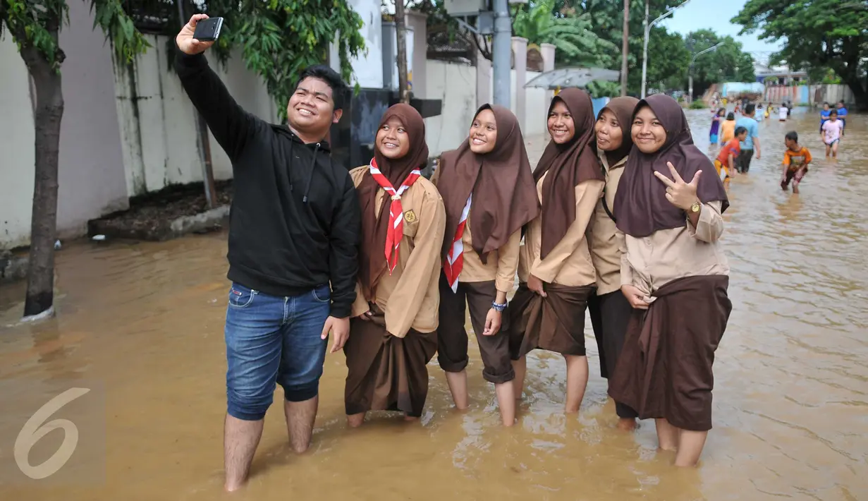 Sejumlah pelajar berfoto di jalanan kawasan Kelurahan Bukit Duri, Tebet, Jakarta yang terendam banjir, Selasa (8/3/2016). Banjir tersebut akibat meluapnya Sungai Ciliwung. (Liputan6.com/Gempur M Surya)