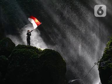 Pengunjung berdiri di atas batu besar sambil memegang bendera Merah Putih di Curug Walet, Pamijahan, Bogor, Jawa Barat, Minggu (24/12/2023). Curug yang terkenal dengan keindahannya ini berada di Desa Ciasihan, Kecamatan Pamijahan. (merdeka.com/Arie Basuki)