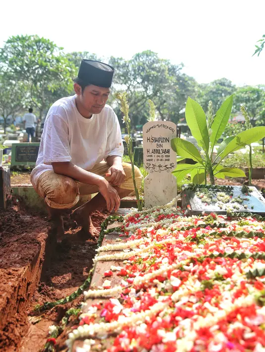 Duduk jongkok di samping nisan sang ayah setelah prosesi pemakaman selesai. Usai pemakaman, Ibnu menceritakan sang ayah meninggal karena penyakit komplikasi. [Foto: Adrian Putra/Fimela.com]
