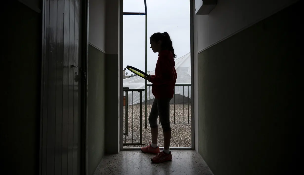 Carola Pessina bersiap bermain tenis dengan Vittoria Oliveri di atap rumah mereka selama lockdown COVID-19 di Finale Ligure, Wilayah Liguria, Italia (19/4/2020). Setiap hari Carola, 11, dan Vittoria, 13, bermain tenis dari satu atap ke atap lain di rumah mereka untuk berlatih. (AFP/Marco Bertorello)