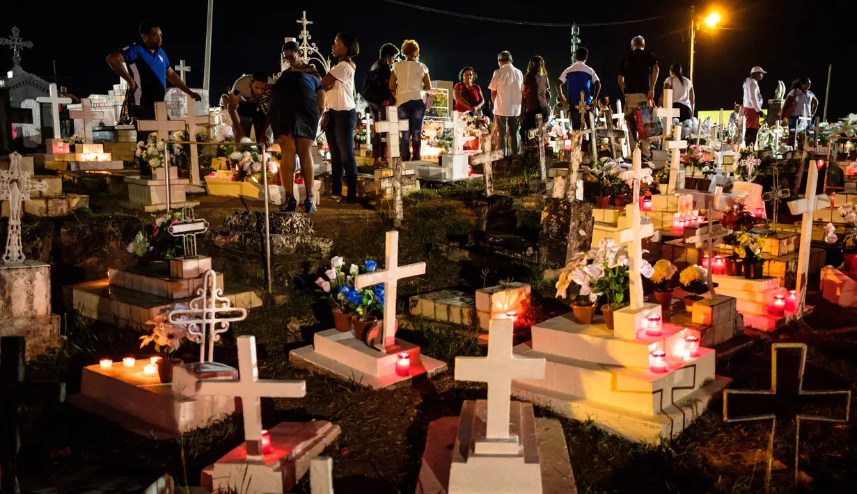Keluarga dan kerabat mengunjungi makam sambil menaruh bunga dan lilin di pemakaman Cayenne di Guyana Prancis (1/11). Mereka mengunjungi makam keluarganya dalam perayaan All Saints Day. (AFP Photo/Jody Amiet)
