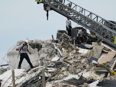 Tim penyelamat berjalan di antara puing-puing dari sebagian menara apartemen tepi laut yang runtuh di Surfside, utara Miami, Kamis (24/6/2021). Runtuhnya gedung apartemen setinggi 12 lantai tersebut mengakibatkan satu orang tewas dan puluhan lainnya masih dinyatakan hilang. (AP Photo/Lynne Sladky)