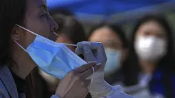 Seorang perempuan memegang maskernya saat tes usap selama pengujian COVID-19 publik di distrik Chaoyang, Beijing, Rabu (11/5/2022). Shanghai pada Rabu menegaskan kembali akan mempertahankan pendekatan &ldquo;nol-COVID&rdquo; pengendalian pandemi, sehari setelah kepala Organisasi Kesehatan Dunia (WHO) menyatakan kebijakan itu tidak berkelanjutan dan mendesak China mengubah strategi. (AP Photo/Andy Wong)