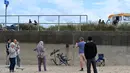 Orang-orang berkumpul untuk melihat karya seni grafiti tikus yang minum koktail, yang menyandang ciri khas seniman jalanan Banksy, di dinding di North Beach di Lowestoft di pantai Timur Inggris pada 8 Agustus 2021. Karya tersebut belum diklaim oleh Banksy. (JUSTIN TALLIS / AFP)