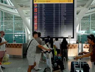 Para penumpang melihat papan elektronik yang menampilkan penerbangan yang dibatalkan di Bandara Internasional Ngurah Rai, Denpasar, Bali, Rabu 13 November 2024. (SONNY TUMBELAKA/AFP)