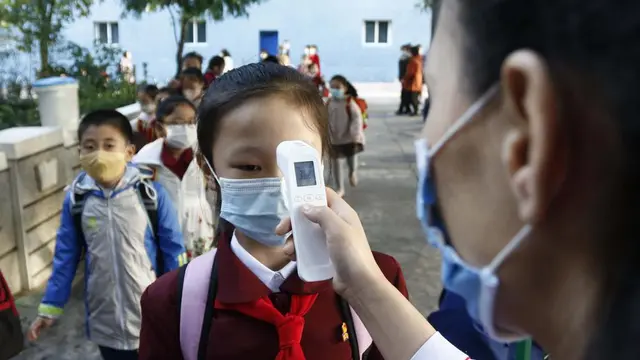 Seorang guru mengukur suhu tubuh seorang siswi untuk membantu mengekang penyebaran virus corona sebelum memasuki Sekolah Dasar Kim Song Ju di Distrik Pusat di Pyongyang, Korea Utara, Rabu, 13 Oktober 2021. (Foto AP/Cha Song Ho, File)