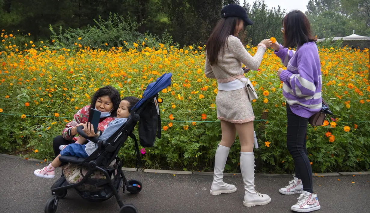 Seorang wanita berfoto dengan seorang anak di dekat bunga yang mekar di taman umum di Beijing, Sabtu (2/10/2021). Pengunjung memadati taman dan lokasi wisata di Beijing saat China merayakan hari kedua masa libur Hari Nasional. (AP Photo/Mark Schiefelbein)