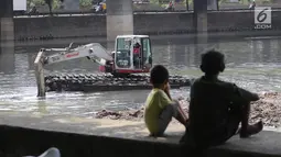Dua bocah melihat proses pengerukan Waduk Grogol, Jakarta, Senin (9/4). Pengerukan dilakukan untuk mengatasi permasalahan banjir di Ibu Kota. (Liputan6.com/Arya Manggala)