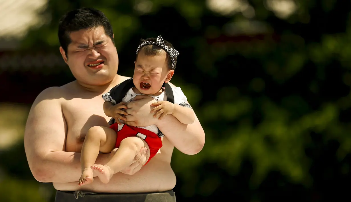 Seorang pegulat sumo amatir ikut menangis saat dia  menggendong bayi yang juga menangis di Tokyo, Jepang, (30/5/2015). Kontes ini merupakan kontes untuk suara bayi dengan tangis yang paling kencang. (REUTERS/Thomas Peter)