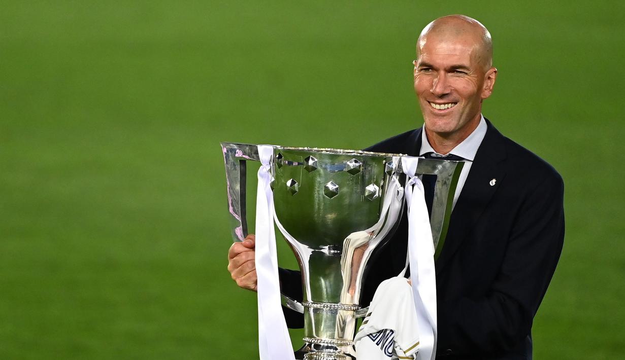 Pelatih Real Madrid, Zinedine Zidane, mengangkat trofi juara La Liga musim 2019/2020 usai timnya mengalahkan Villarreal pada laga lanjutan La liga di Estadio Alfredo Di Stefano, Jumat (17/7/2020) dini hari WIB. (AFP/Gabriel Bouys)