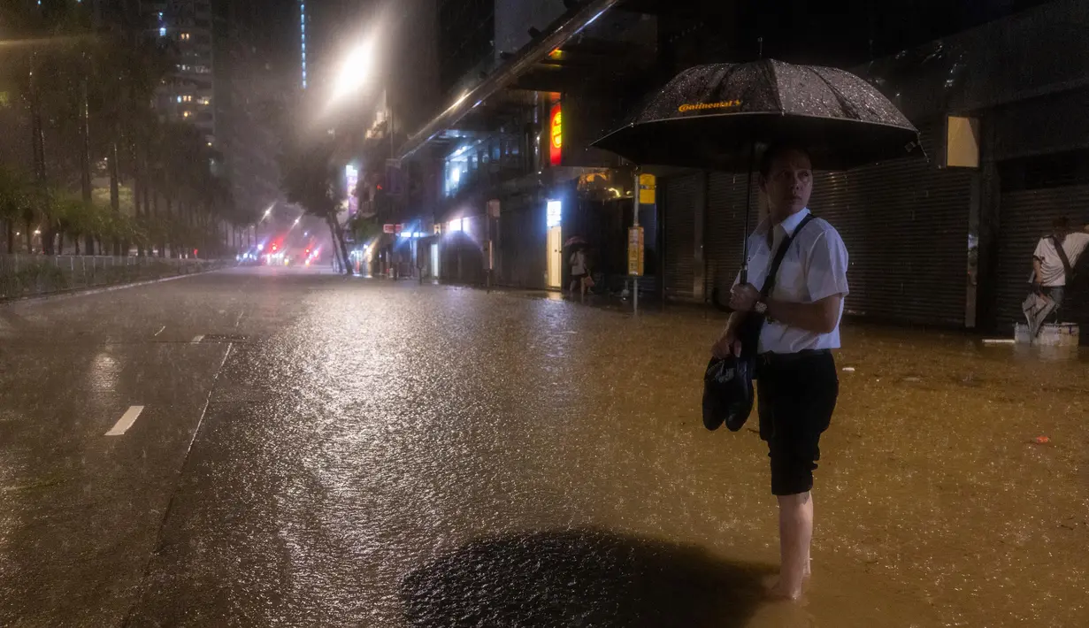 Banjir bandang melanda sejumlah wilayah di Hong Kong. Tampak seorang pejalan kaki menunggu bus di jalan yang tergenang air setelah hujan deras di Hong Kong, Jumat, 8 September 2023. (AP Photo/Louise Delmotte)