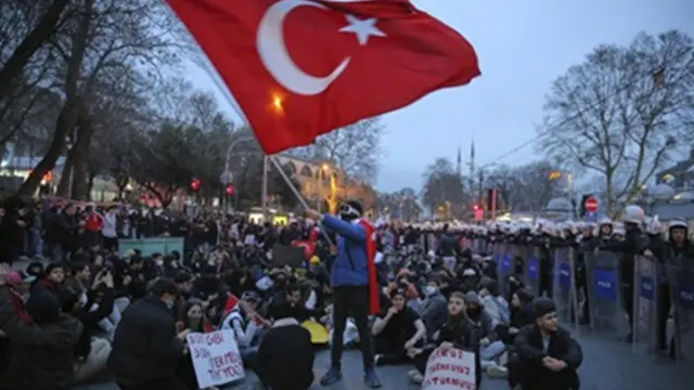 Sejumlah mahasiswa duduk di samping petugas polisi anti huru hara di Istanbul, Turki, pada Senin (24/3/2025), saat protes pasca penangkapan Wali Kota Istanbul Ekrem Imamoglu.