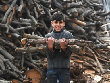 Seorang anak laki-laki menggotong kayu bakar di sebuah bengkel kerja di Damaskus, ibu kota Suriah, pada 23 November 2020. Warga Suriah mengumpulkan kayu bakar untuk menghadapi cuaca dingin. (Xinhua/Ammar Safarjalani)
