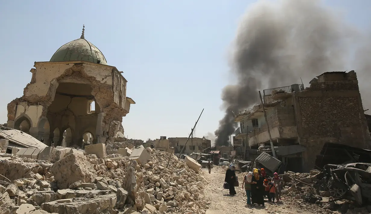 Warga sipil Irak melewati Masjid Agung al-Nuri yang hancur saat mengungsi dari Kota Tua di Mosul, 30 Juni 2017. Masjid yang dibangun pada abad ke-12 ini diledakkan ISIS pada 21 Juni 2017 sebagai upaya menghambat laju pasukan Irak. (AHMAD AL-RUBAYE/AFP)