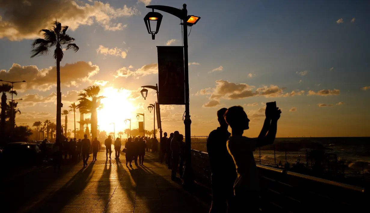 Orang-orang mengambil gambar terjangan ombak saat matahari terbenam di sepanjang garis pantai Beirut, Lebanon (26/10).  (AP Photo / Hassan Ammar)